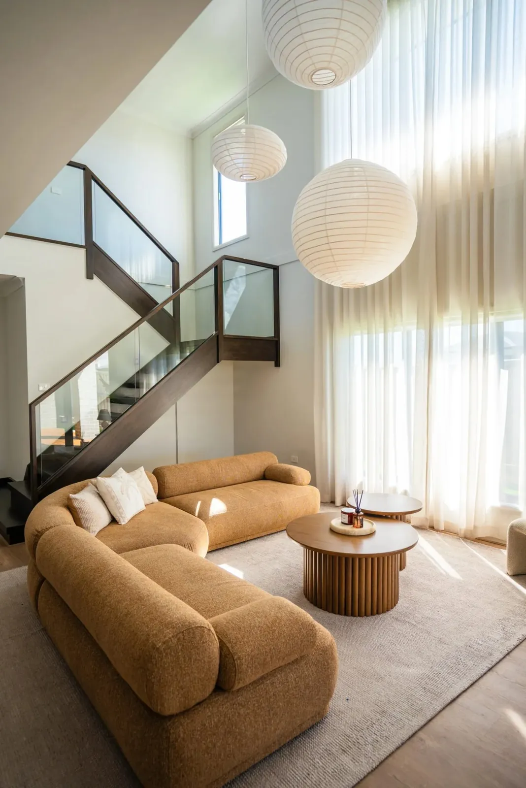 Cozy Retreat double-height living room with paper lanterns, sheer curtains and a curved ochre sofa