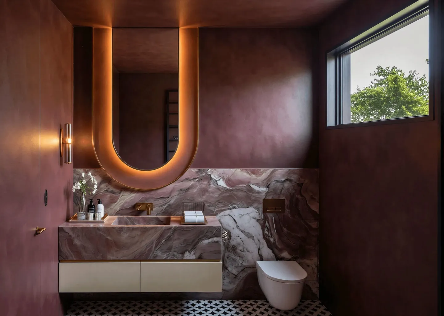 Spanish Reverie bathroom with burgundy walls, veined stone and a curved backlit mirror