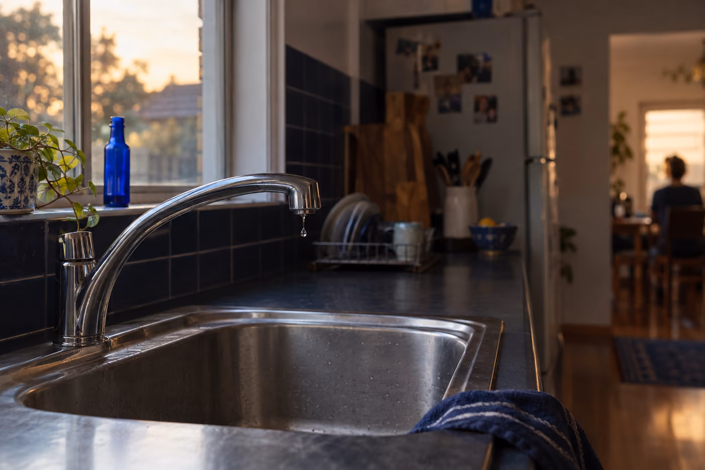 A kitchen tap dripping into a stainless steel sink in soft evening light